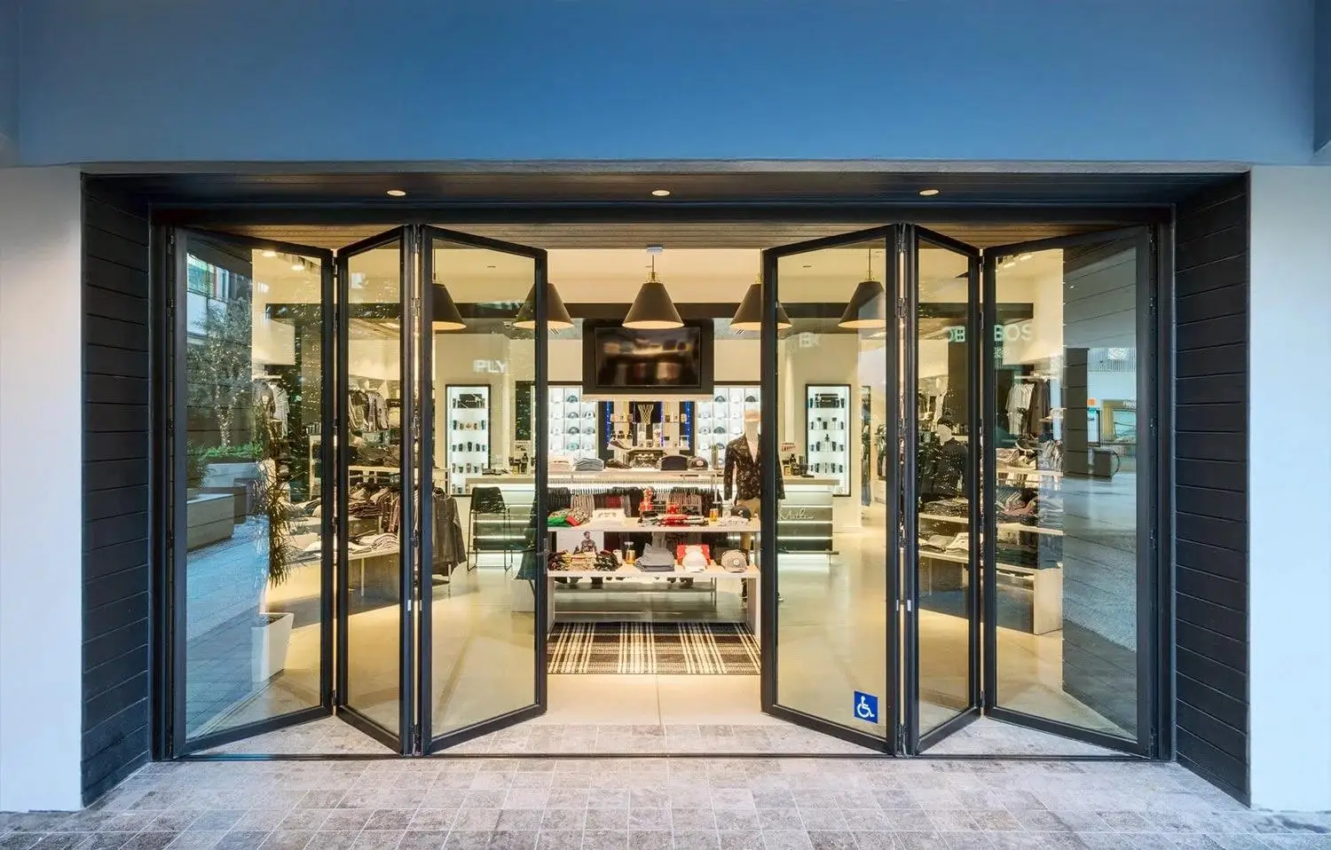 Black commercial aluminum folding doors fully opened at a modern retail storefront, showcasing heavy-duty glass panels, seamless customer flow, and ADA-compliant design.