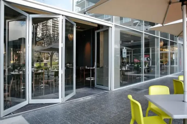Aluminum bifold storefront doors opening a commercial cafe interior to outdoor patio seating.