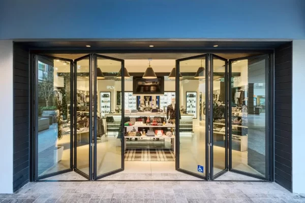 Black commercial aluminum folding doors fully opened at a modern retail storefront, showcasing heavy-duty glass panels, seamless customer flow, and ADA-compliant design.